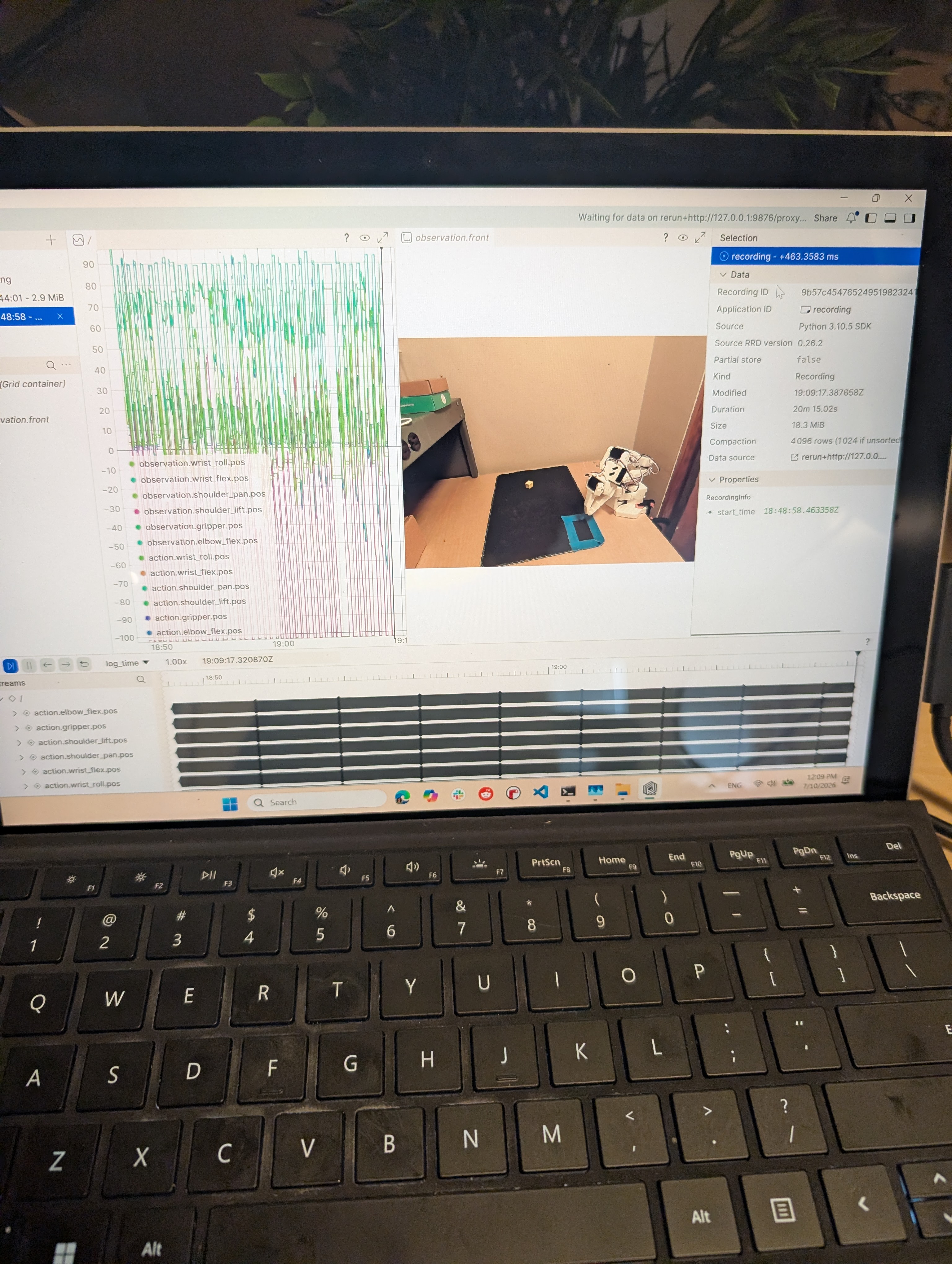 Laptop showing a terminal encoding episodes next to the Rerun viewer with joint/action plots and the front camera feed